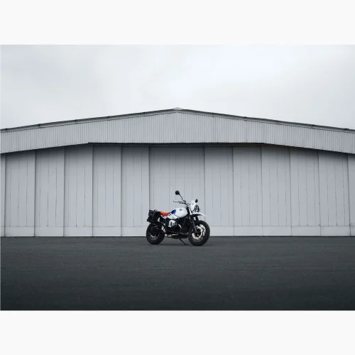Tirage intitulé Flat Twin Hangar qui représente une BMW Nine T Urban GS devant un hangar d'avion.